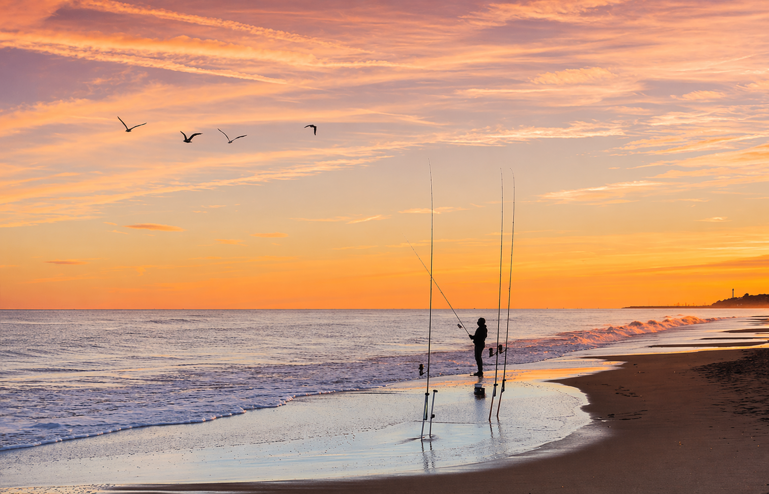 Lone fisherman silhouetted against a beach sunset
